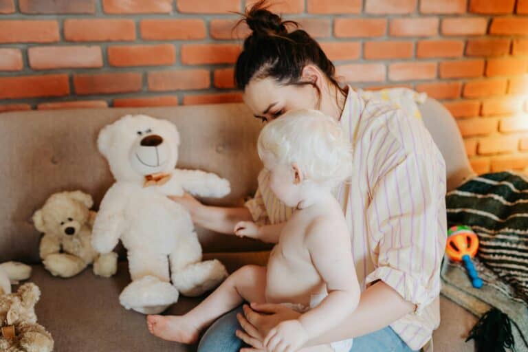 Woman and a baby sat on a sofa looking at a teddy bear
