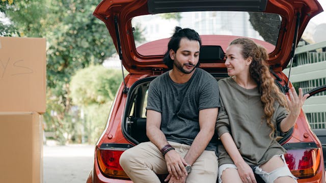 A man and a woman sat closely in the open boot of a red car